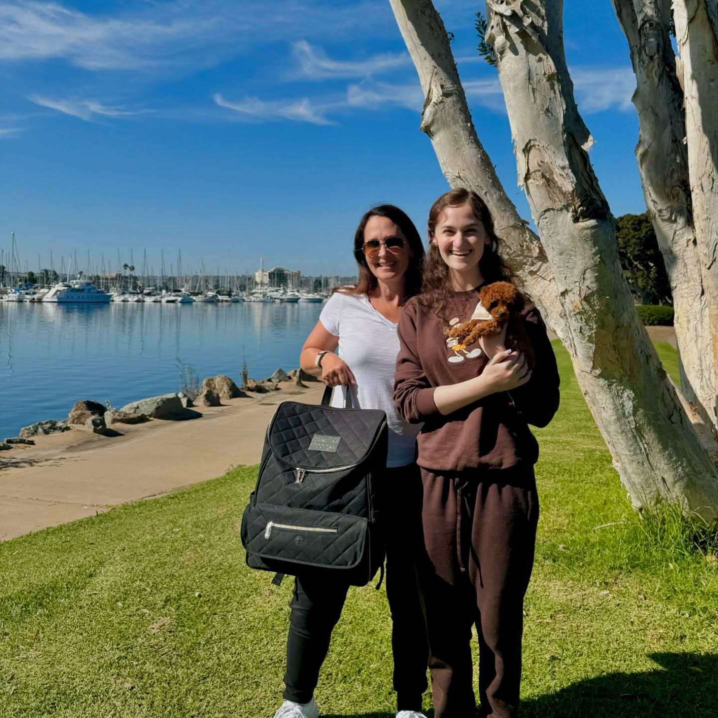 Two people by a waterfront, one holding a small brown puppy