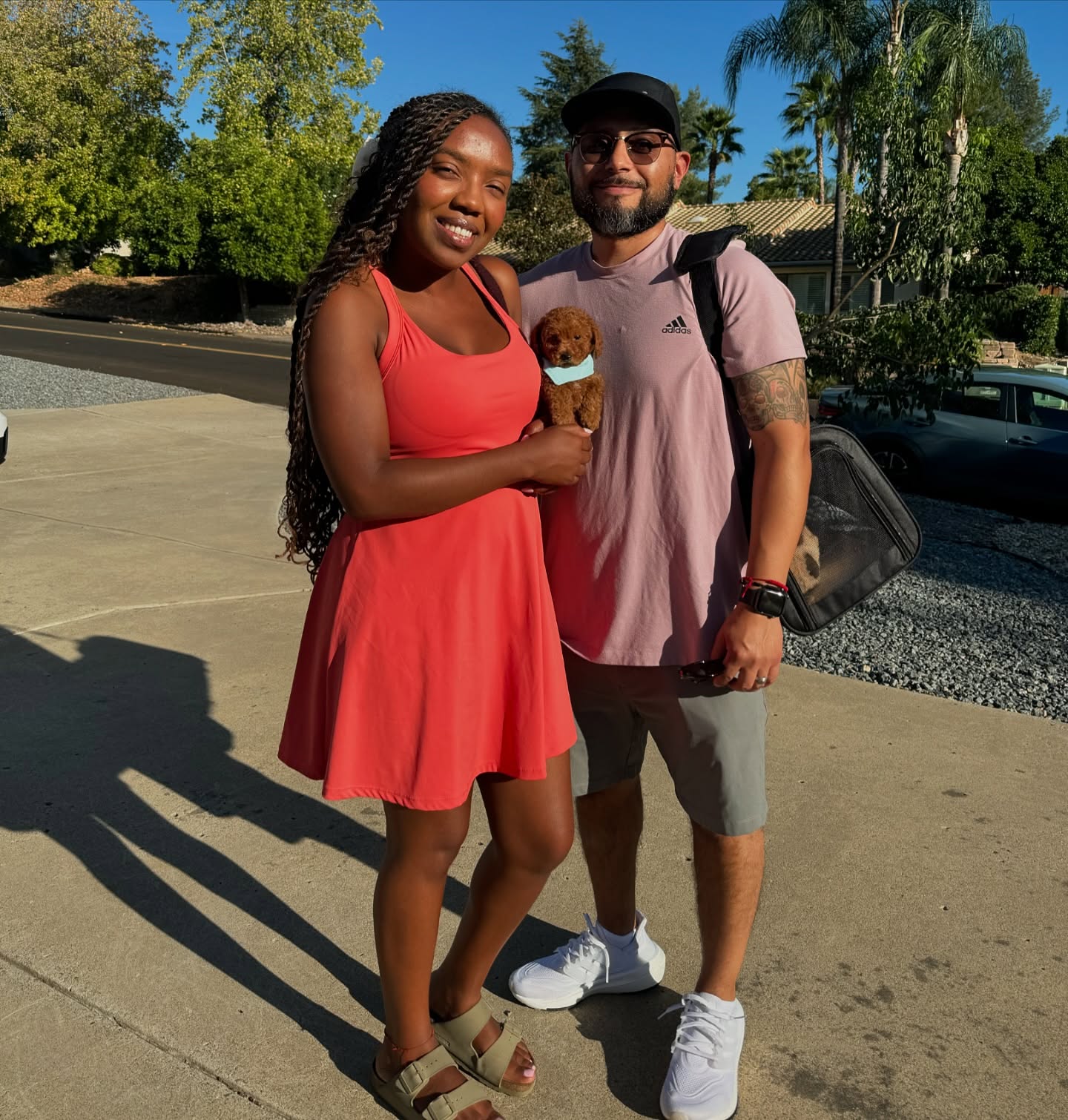 Two adults standing outdoors while one holds a small brown puppy